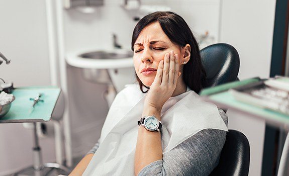 Woman holding cheek during root canal treatment appointment