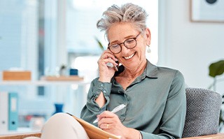 Woman smiling while talking on phone and taking notes