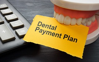 Artificial teeth biting yellow paper that says “Dental Payment Plan”