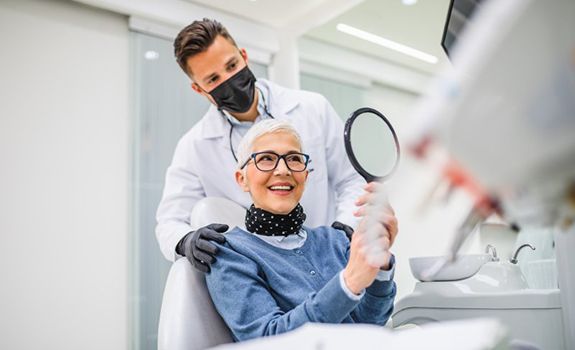 Patient smiling into mirror while dentist stands nearby