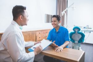 dentist and patient talking with a dental chair in the background